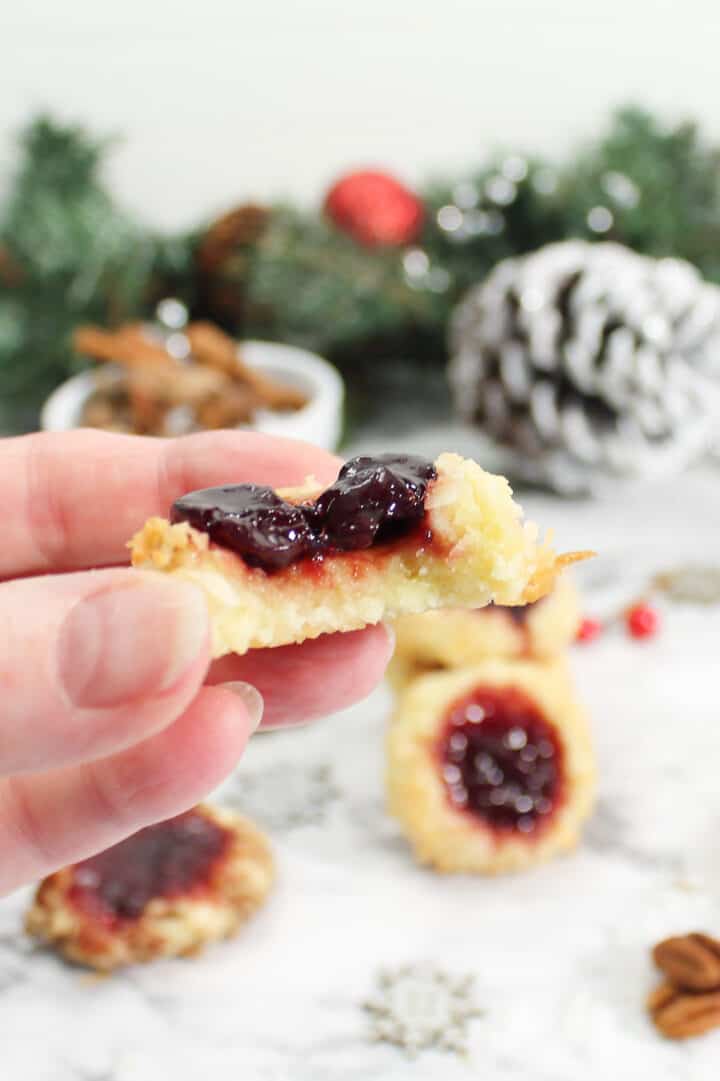 Holding shortbread cookie with jam with bite out of it.
