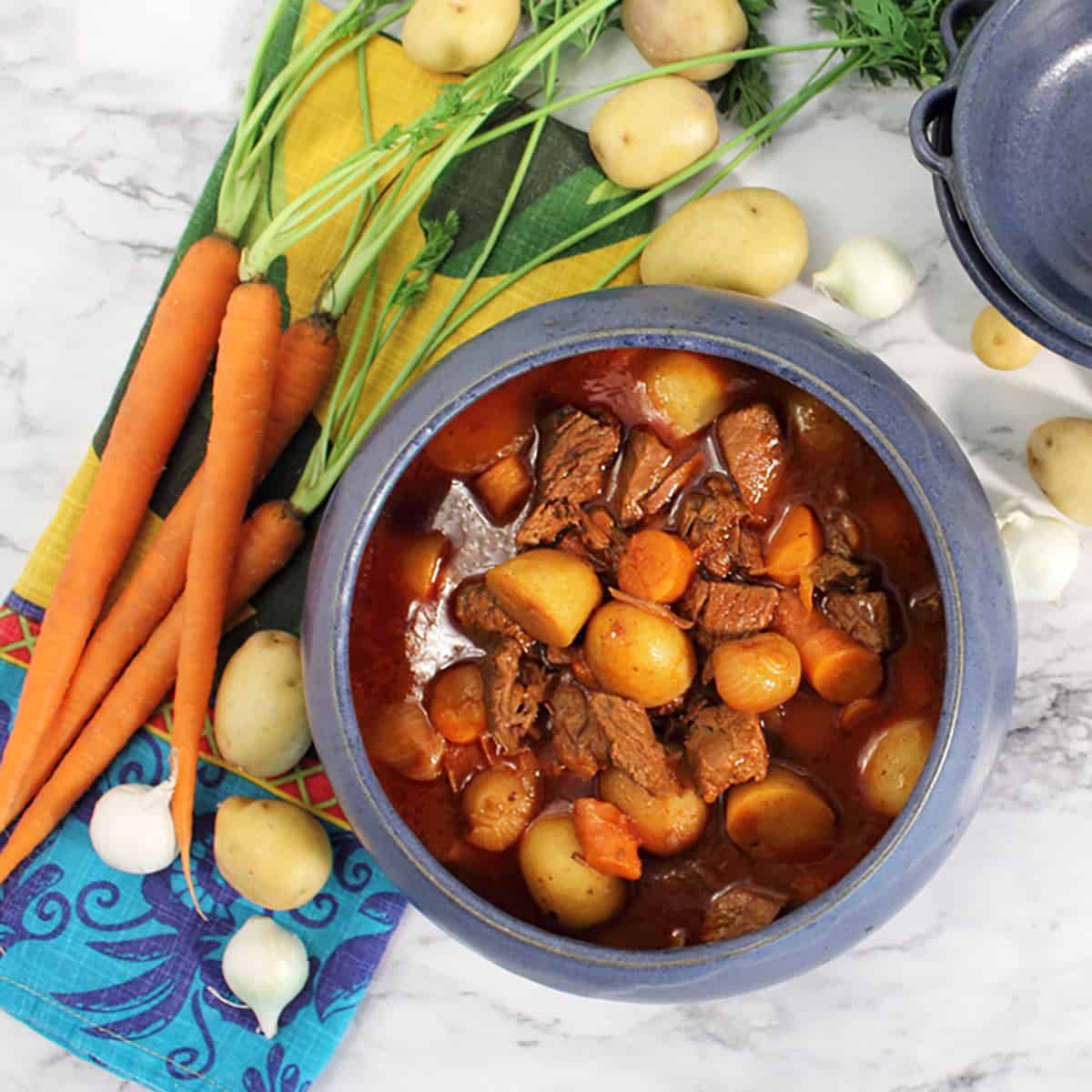 Overhead of stidfado in blue bowl with carrots and potatoes around it.