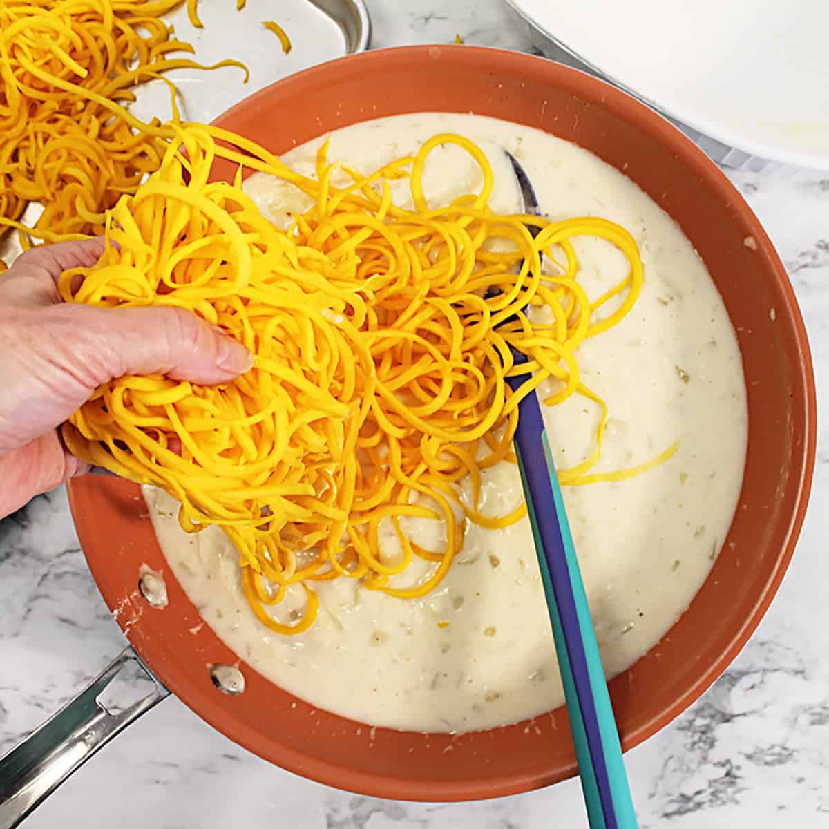 Putting handful of squash noodles in cream sauce.