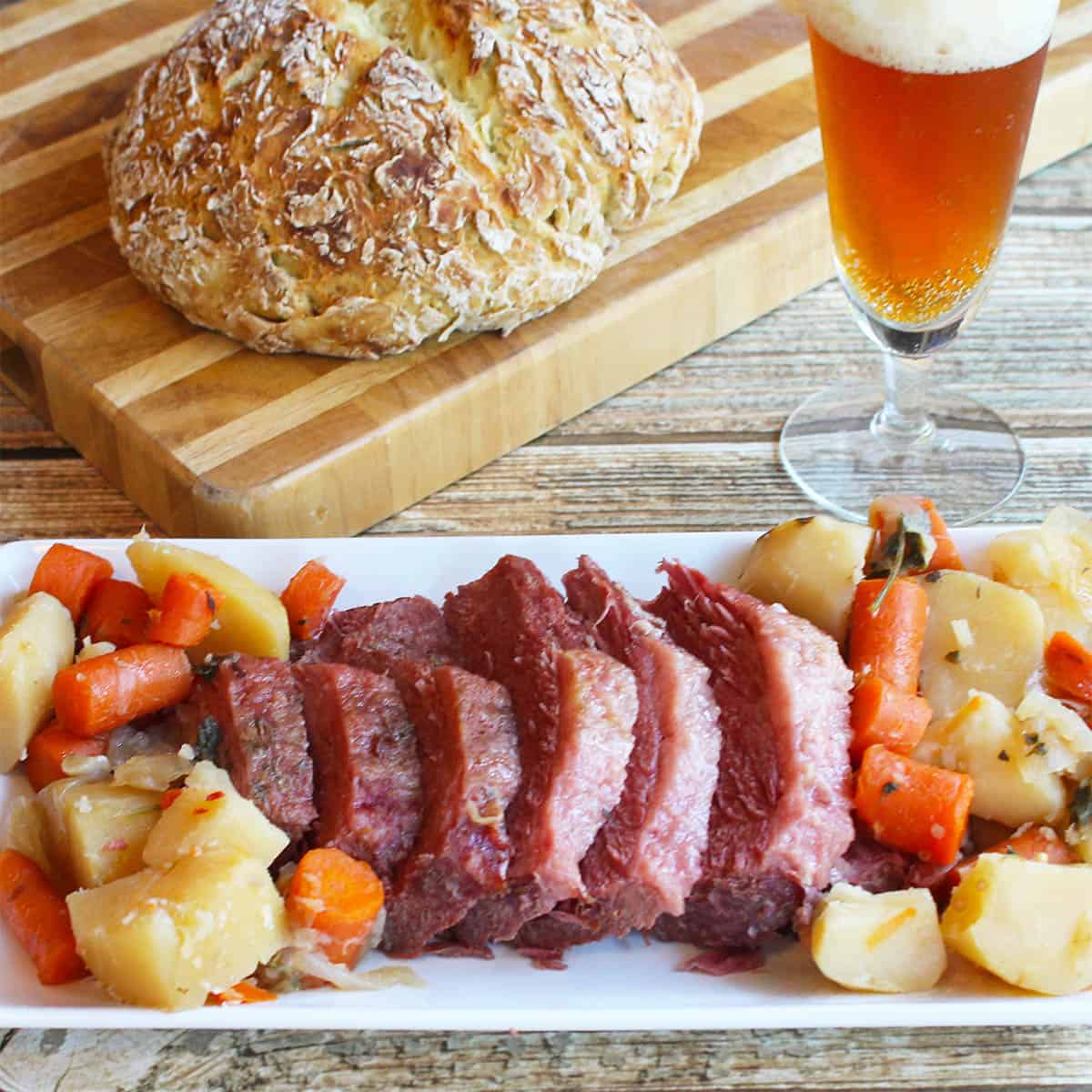 Corned beef dinner on platter with beer and Irish soda bread in background.