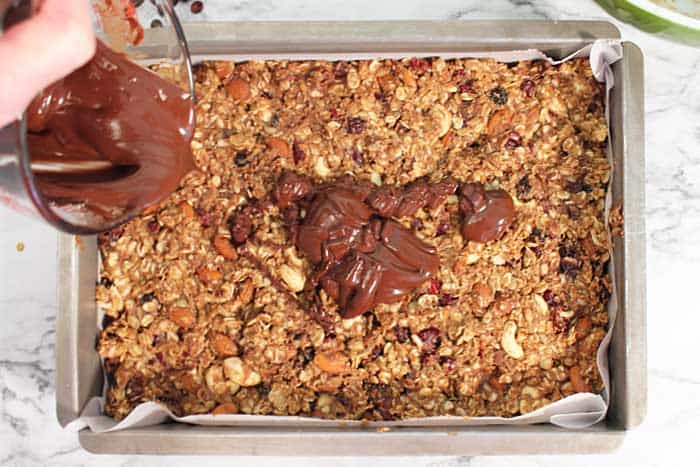 pouring melted chocolate on top of granola bars