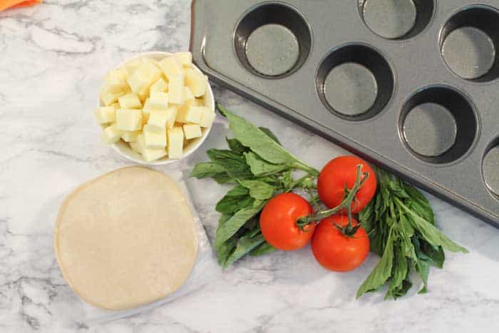 Tomatoes, basil, cubed mozzarella and empanada discs on table by muffin pan