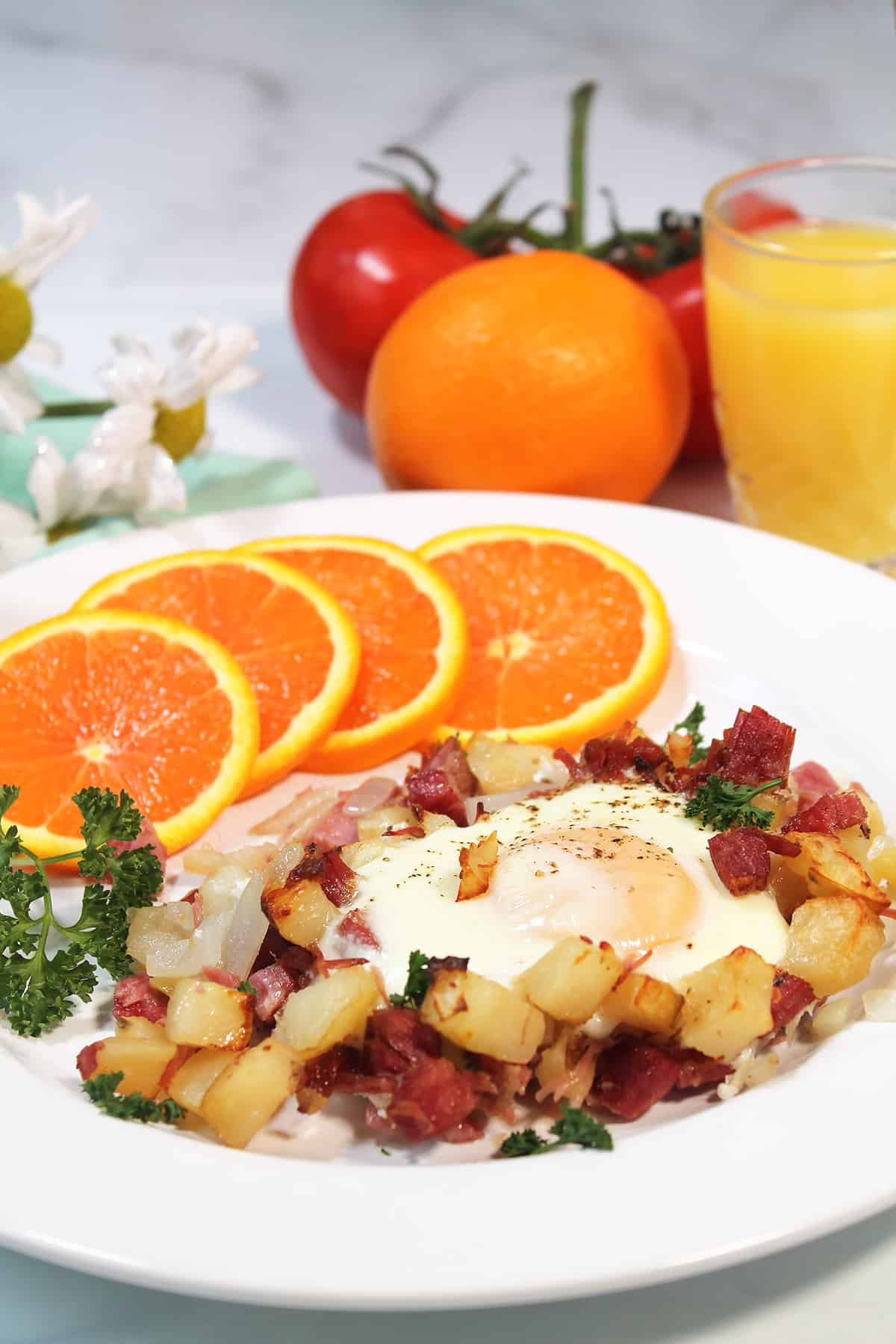 Plated Corned Beef Hash and eggs with orange slices and orange juice.