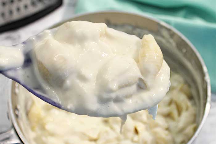 Spoonful of creamy mac and cheese above saucepan