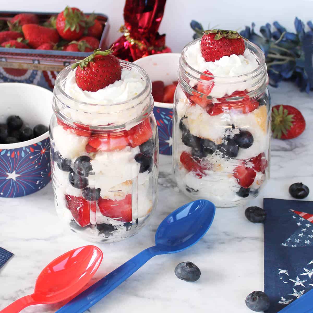 2 Patriotic Parfaits ready to serve with colored spoons and berries around.