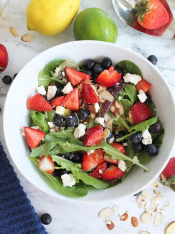 Overhead of Mixed Berry Salad in white bowl with fruit and nuts scattered around.