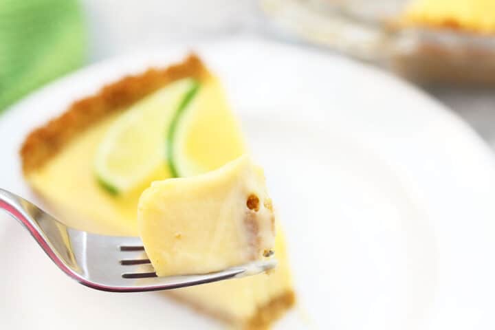 Bite of key lime pie on fork over slice.