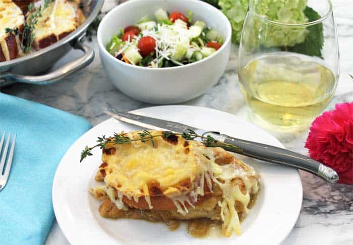 Plated French Onion Chicken on white plate with salad and wine in background.