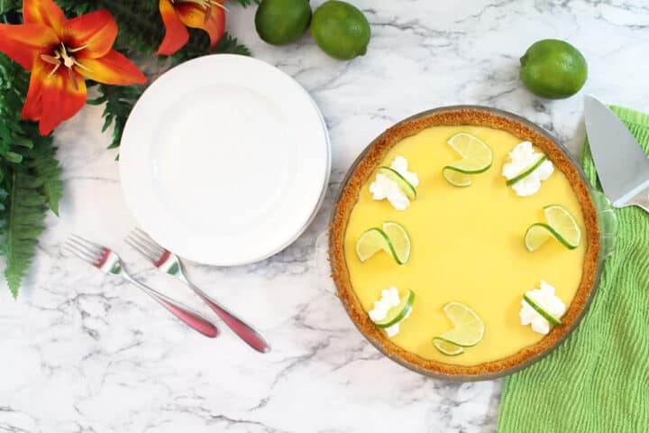 Overhead of decorated pie on marble table next to serving plates.