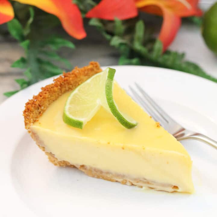 Slice of key lime pie on white plate in front of flowers.