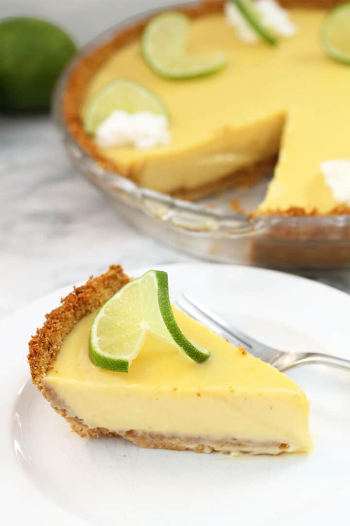 Slice of pie with fork on white plate in front of whole pie.