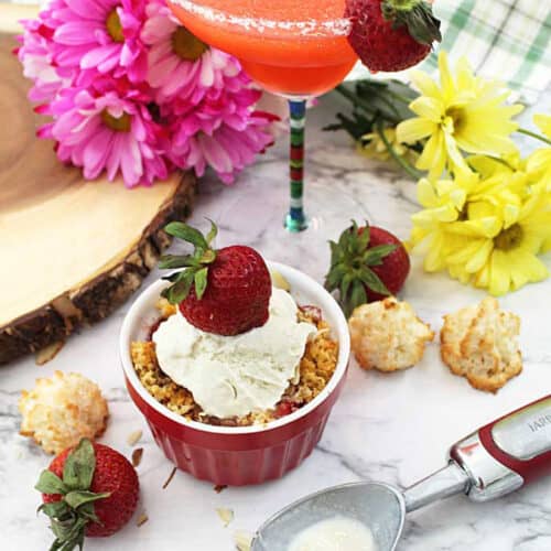 Strawberry Crisp with ice cream on white table with margarita in background.
