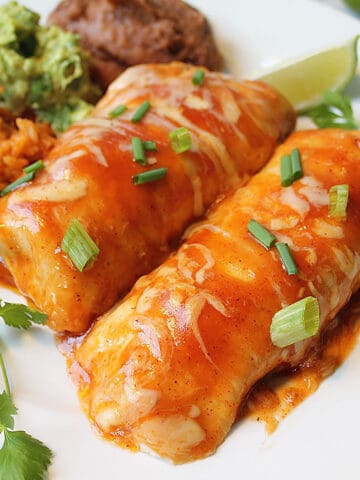 Closeup of enchiladas on white plate with lime slice rice guacamole and beans.