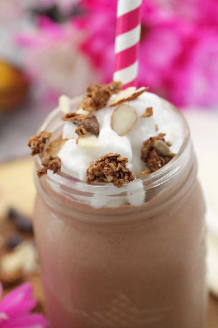 Closeup of smoothie with whipped cream and granola with red striped straw.