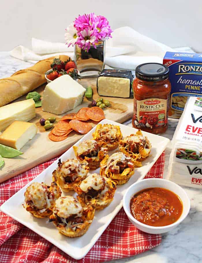 Appetizer spread with pasta sauce and penne packaging and flowers.