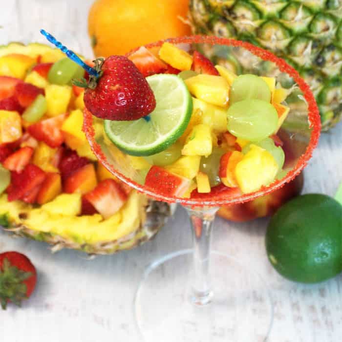 single fruit cocktail in martini glass with lime and strawberry garnish.