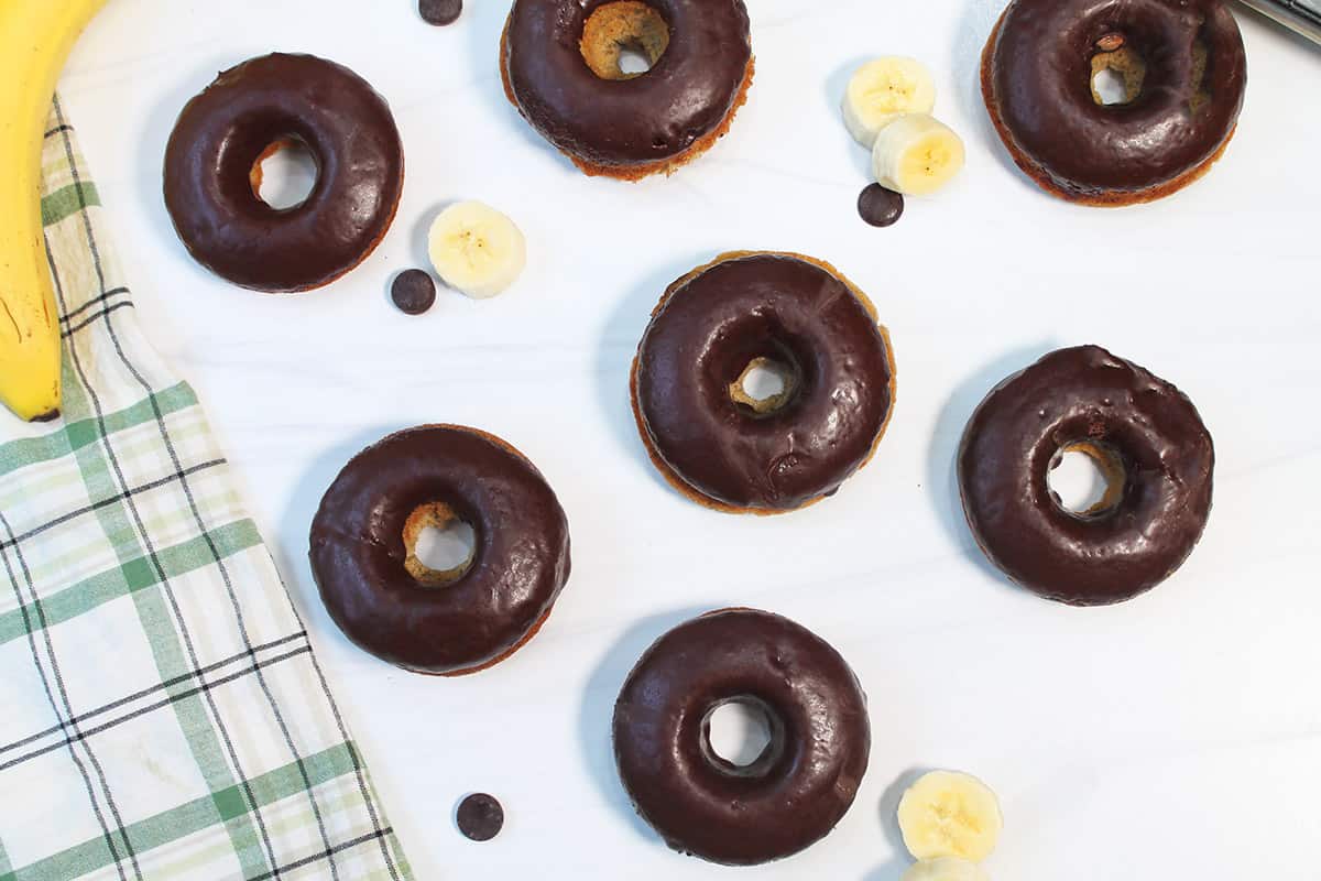 Overhead of baked donuts with chocolate glaze on white table.