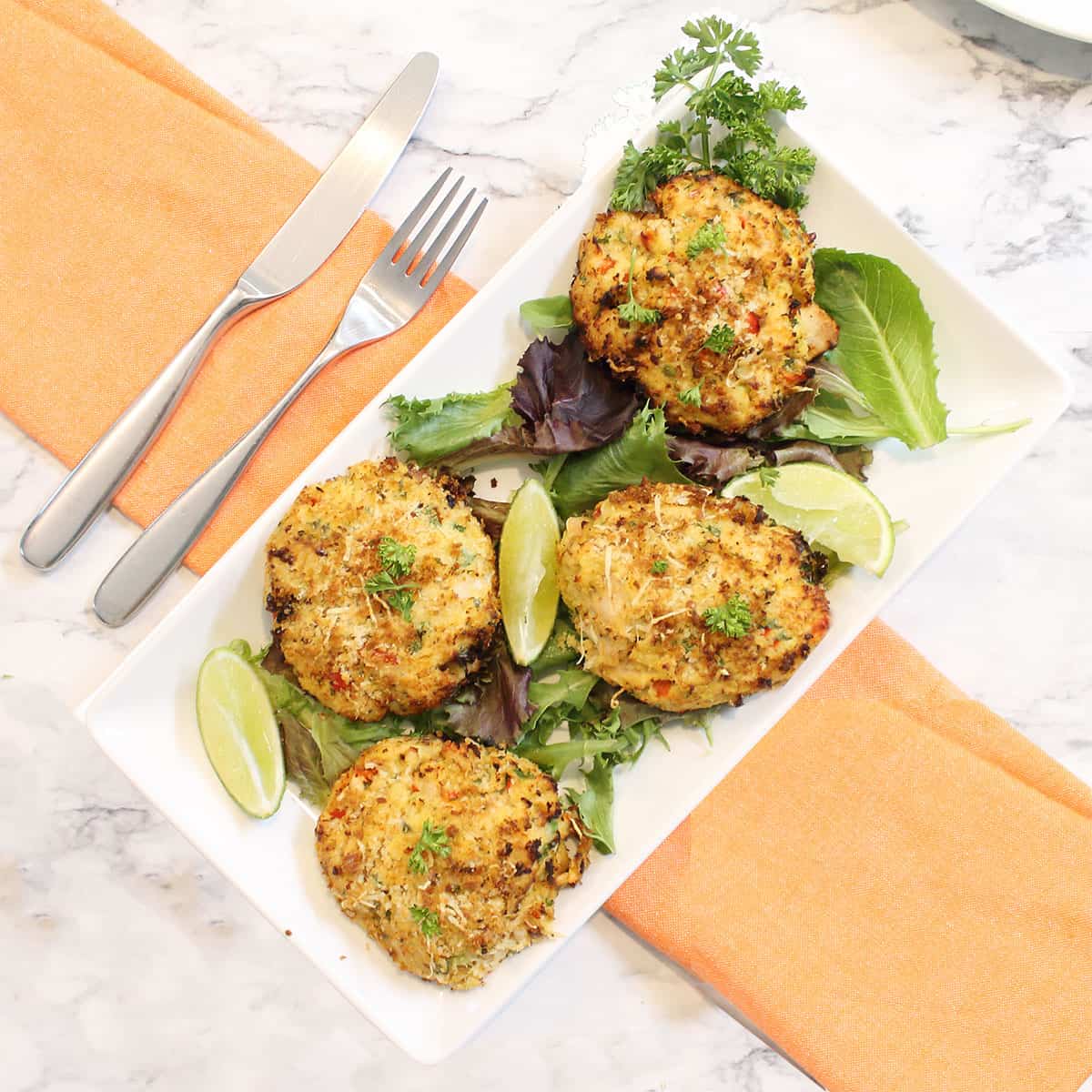 Air fried tuna fish patties on white platter on top of peach napkin.