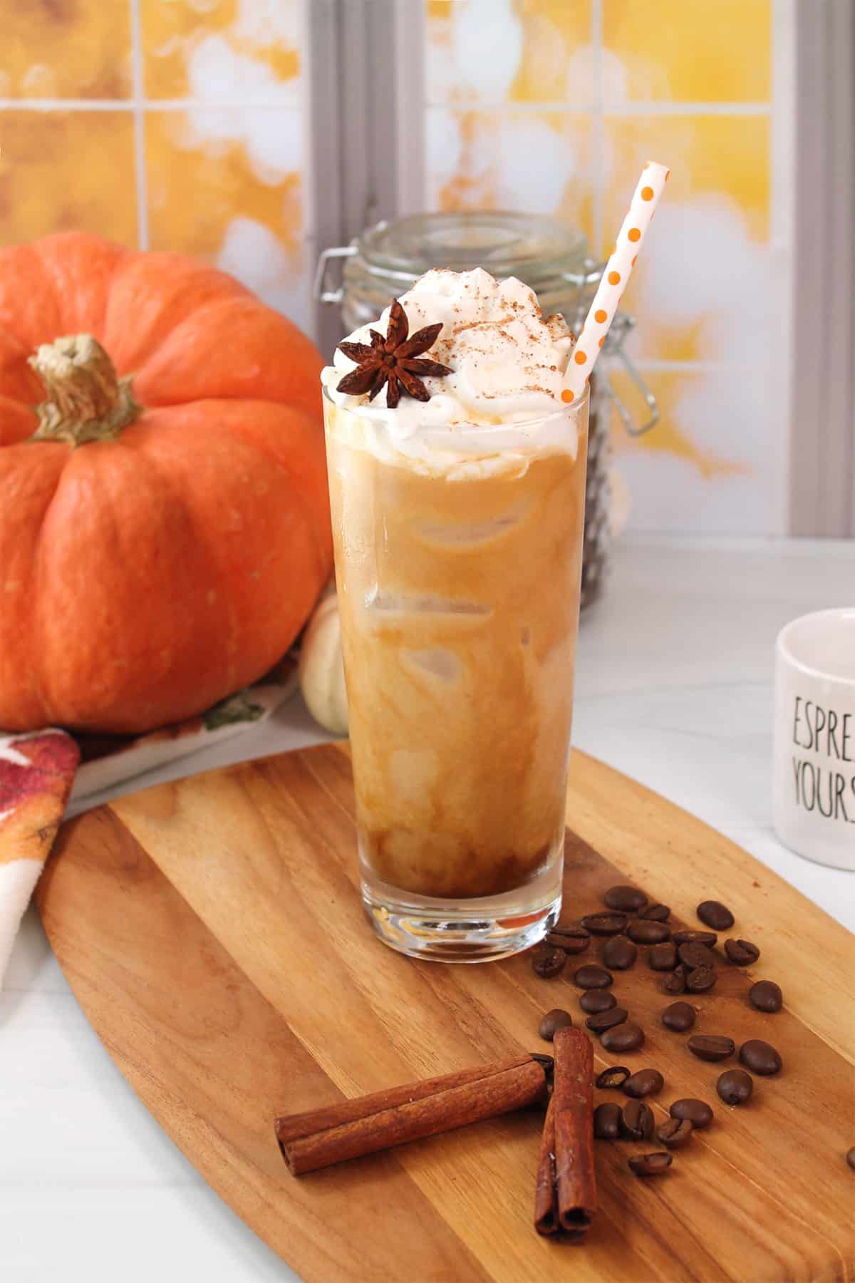 Iced Pumpkin Spice Latte with straw next to pumpkin.
