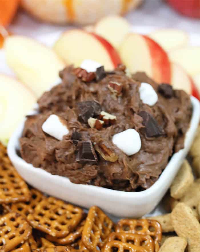 Closeup of cookie dough dip in white bowl with apple dippers in background.