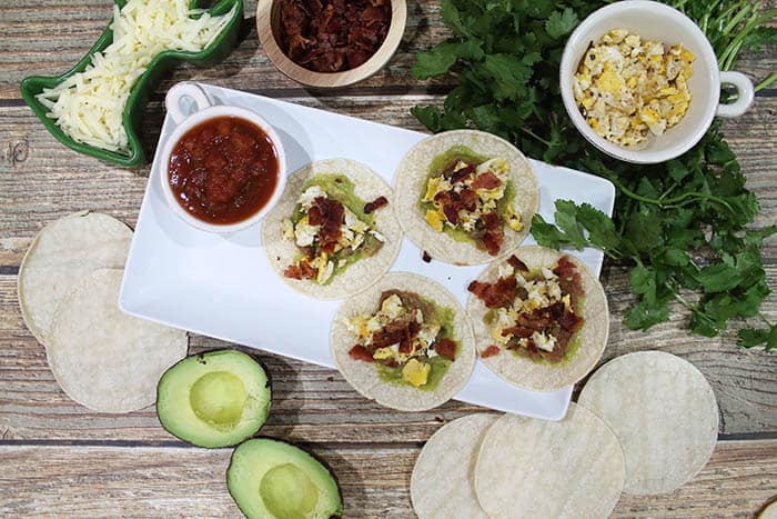 Sprinkles of bacon on open breakfast tacos.