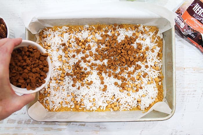 Sprinkling cinnamon chips over coconut layer.