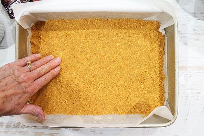 Patting graham crackers into prepared pan.