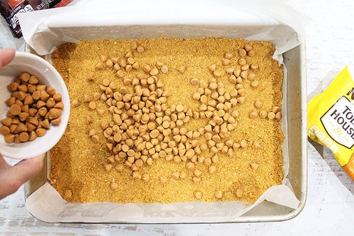 Sprinkling butterscotch chips over graham cracker base.