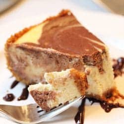 Bite on fork with piece of cheesecake on white plate.