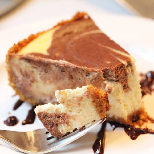 Bite on fork with piece of cheesecake on white plate.