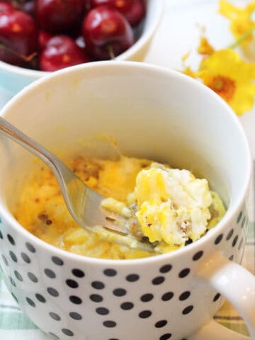 Spoonful of egg breakfast with cherries and yellow flowers.