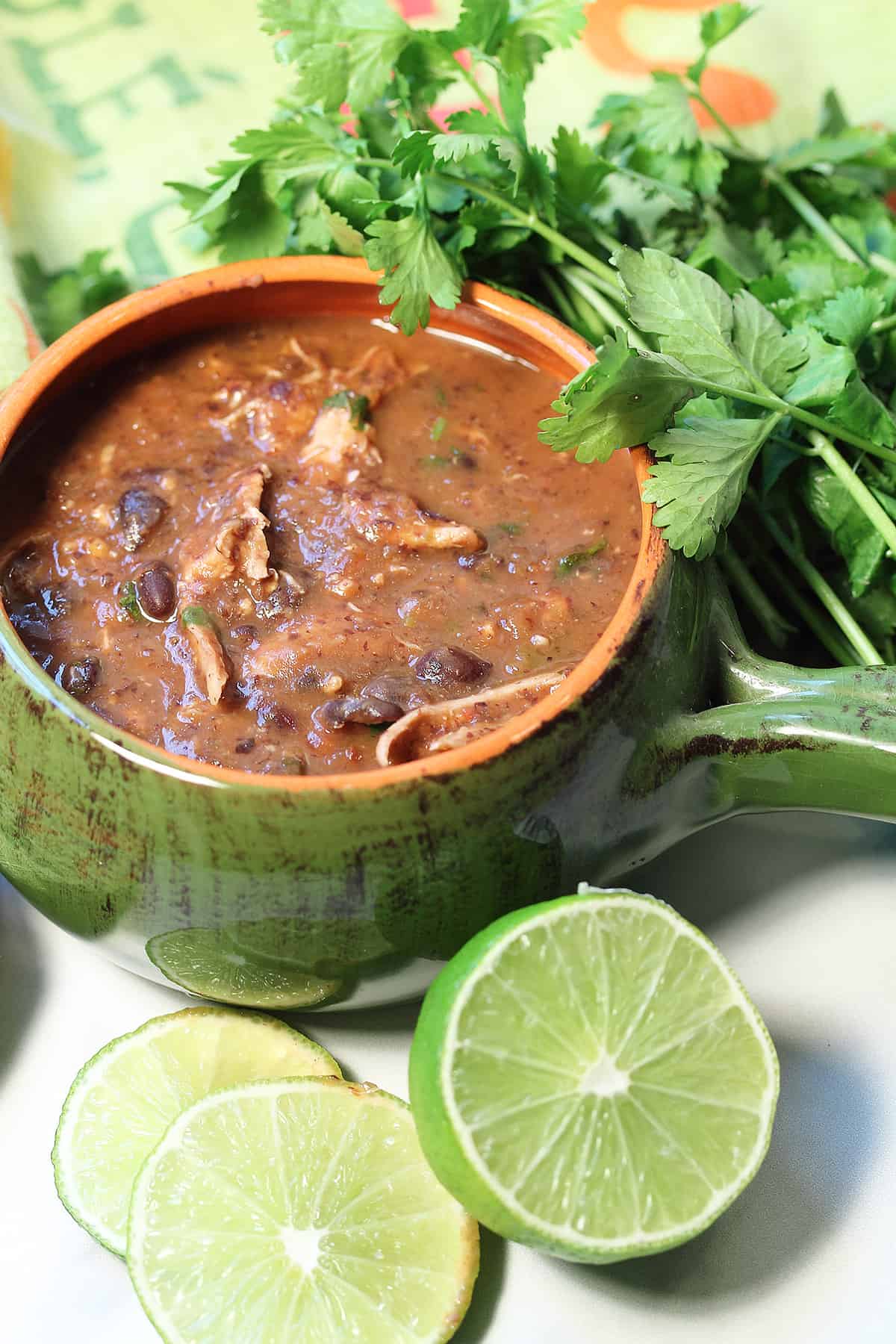 Green bowl of chicken black bean soup with lime and cilantro.