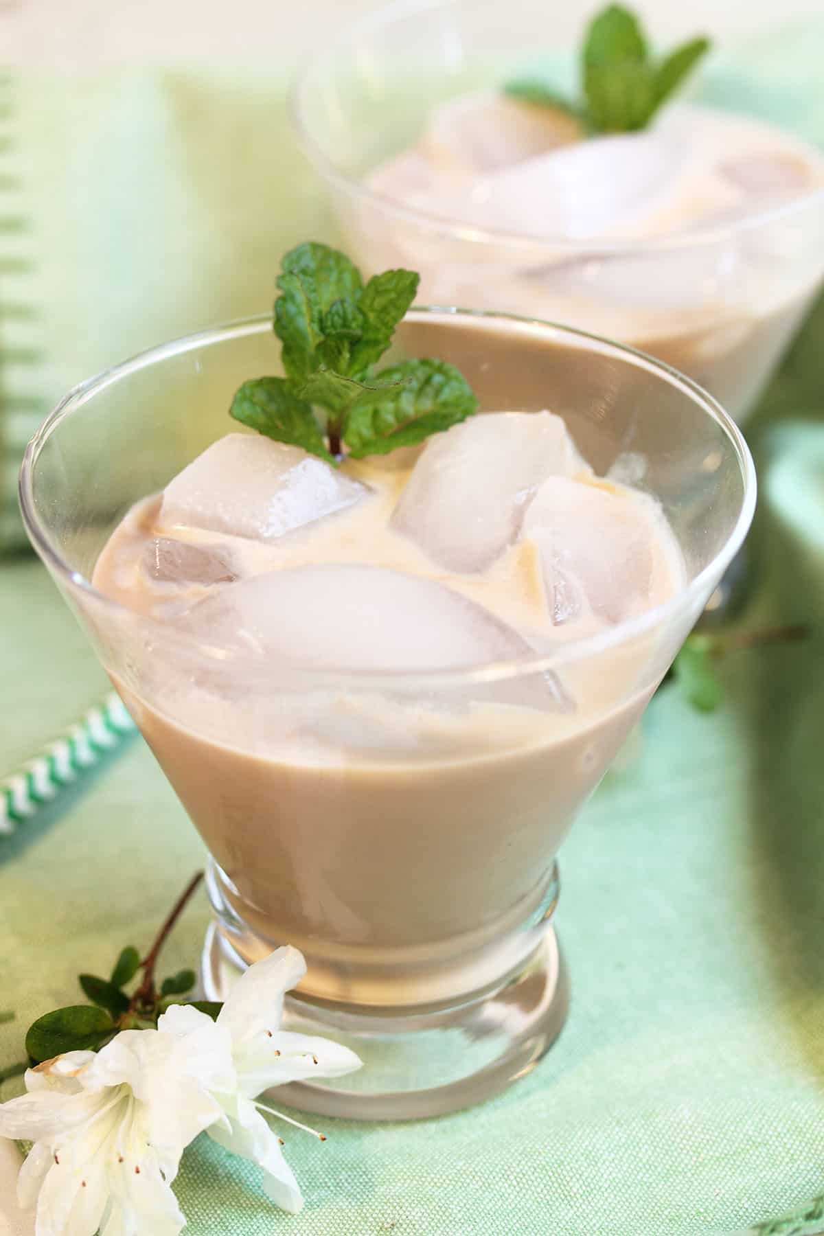 2 glasses of irish cream on the rocks with white azaleas ad striped green straw.