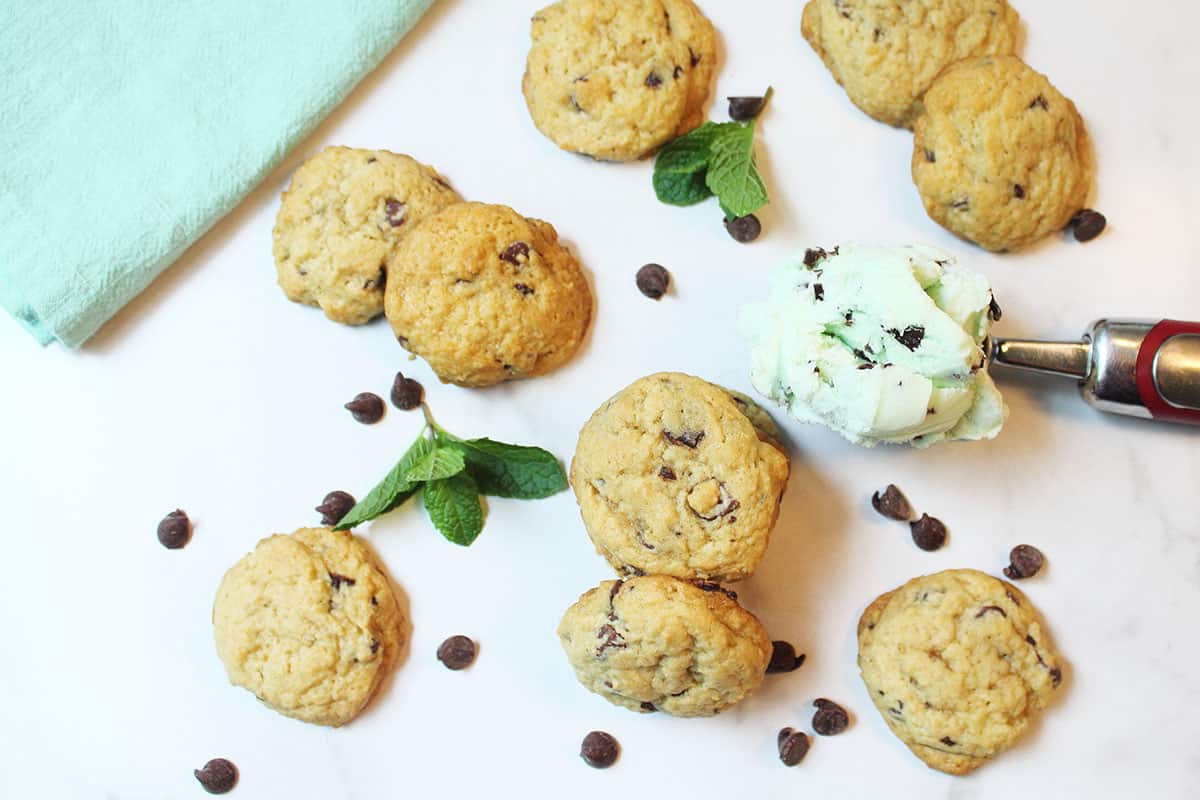 Scattered cookies among mint leaves chocolaet chips and scoop of ice cream.