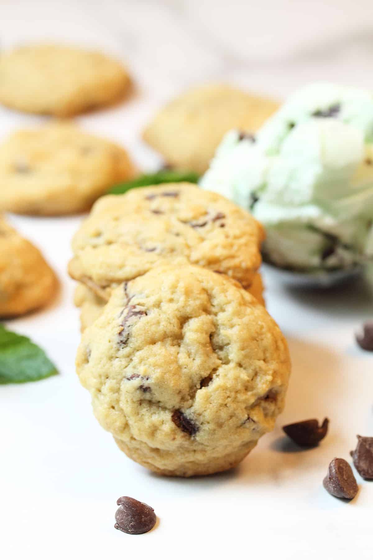 Single cookie leaning on stacked cookies with ice cream in background.