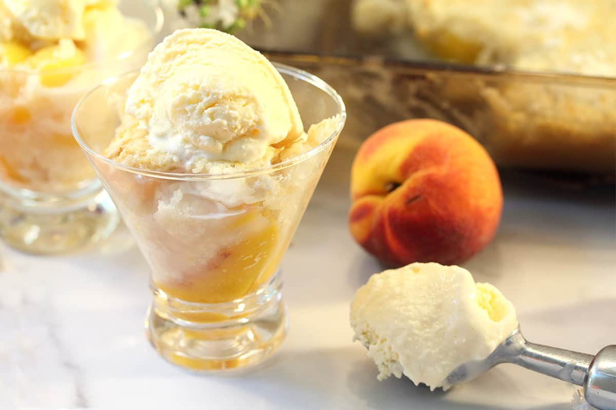 Peach Cobbler in glass dish with scoop of ice cream on side.