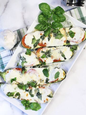 Zucchini boats on white plate with green plaid towel on side.