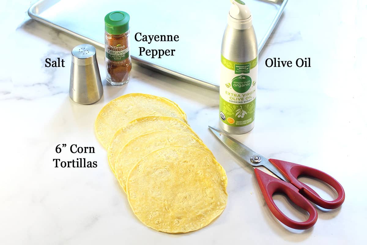 Ingredients - tortillas, salt, cayenne and olive oil spray laid out on white table with pair of kitchen shears.