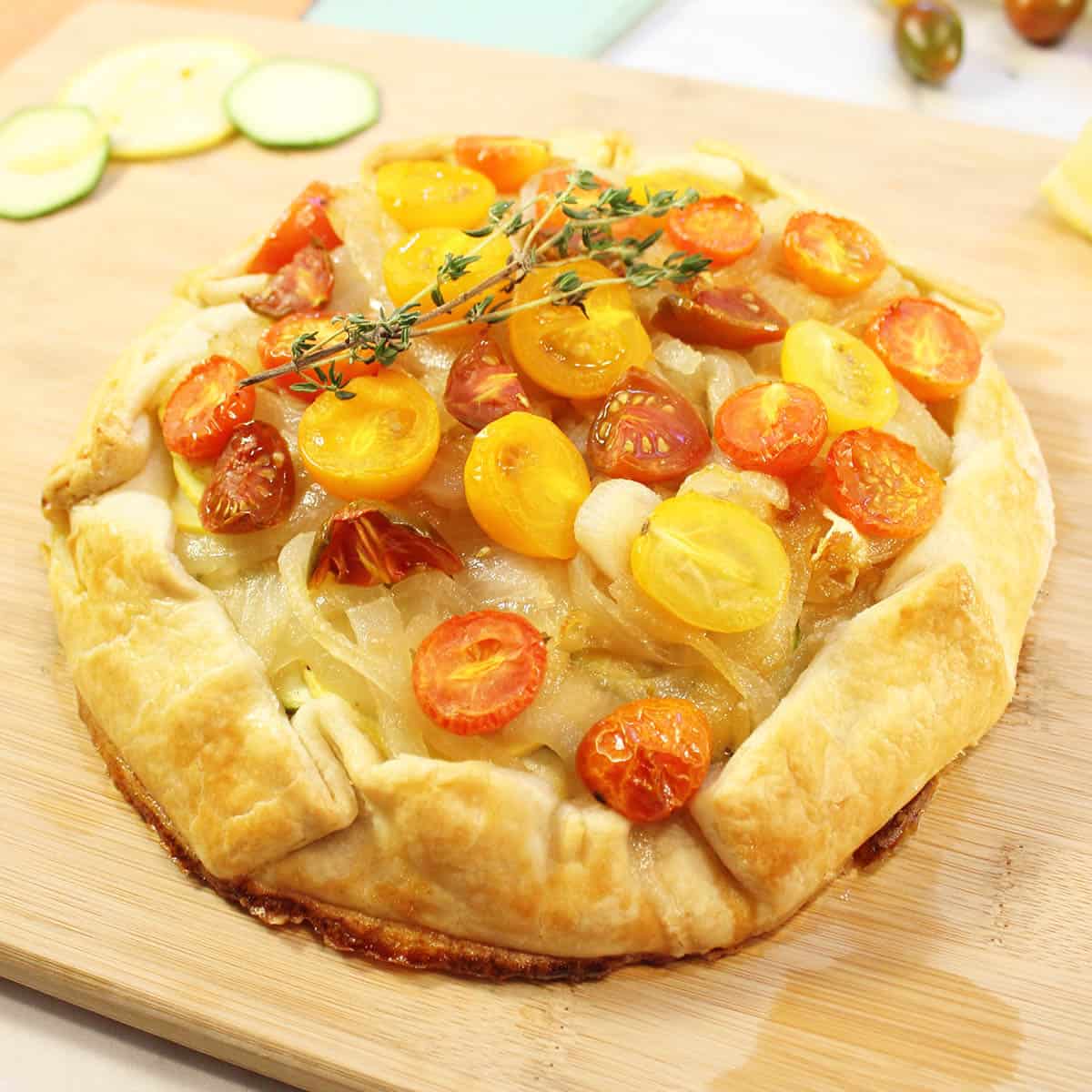 Closeup of browned squash galette on wooden board with thyme garnish on top.
