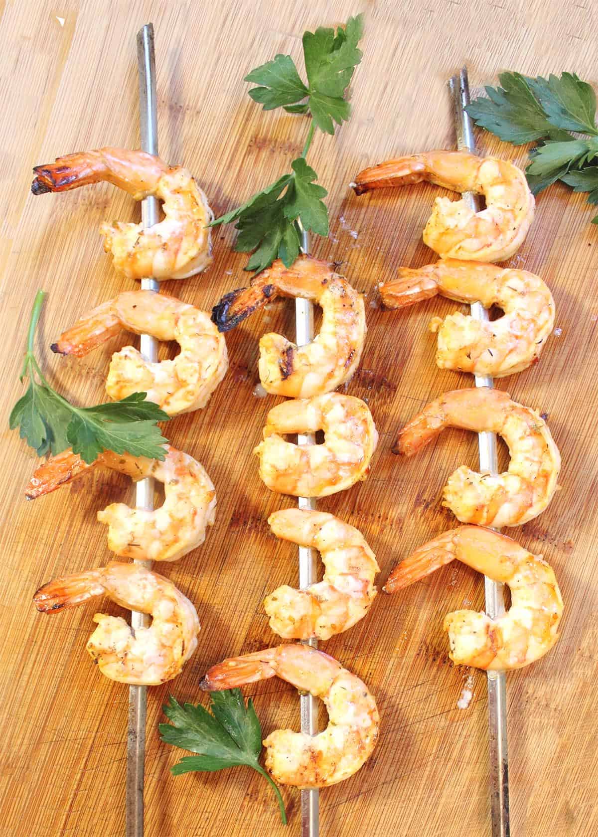 Three grilled shrimp skewers on wooden board.