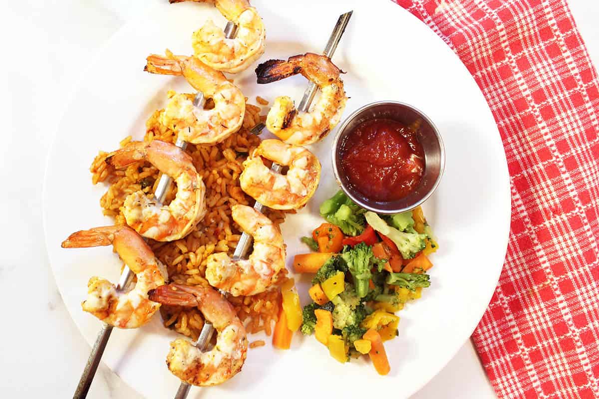 Plated dinner of shrimp on top of rice with vegetables.