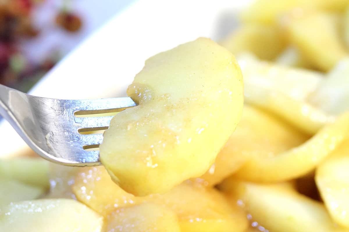 Bite of apple on fork over serving dish.