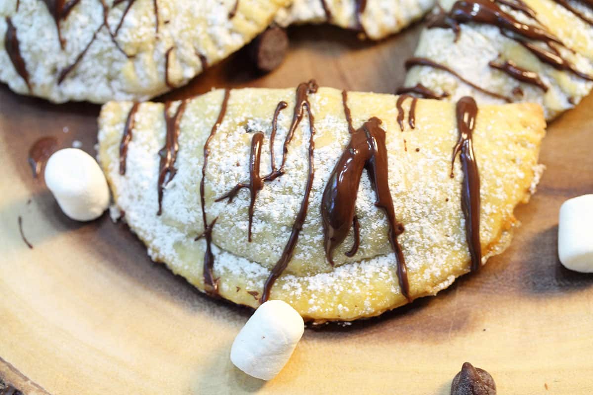 Closeup of baked empanada with powdered sugar and chocolate drizzle.