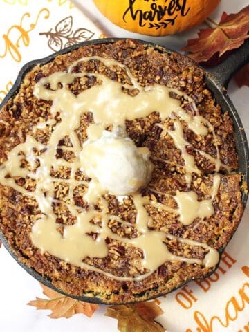 Overhead of baked pumpkin cobbler with scoop of ice cream on top and drizzle of maple sauce.