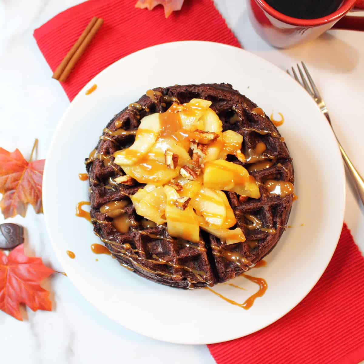 Overhead of waffles on white plate topped with apples with red napkin underneath.