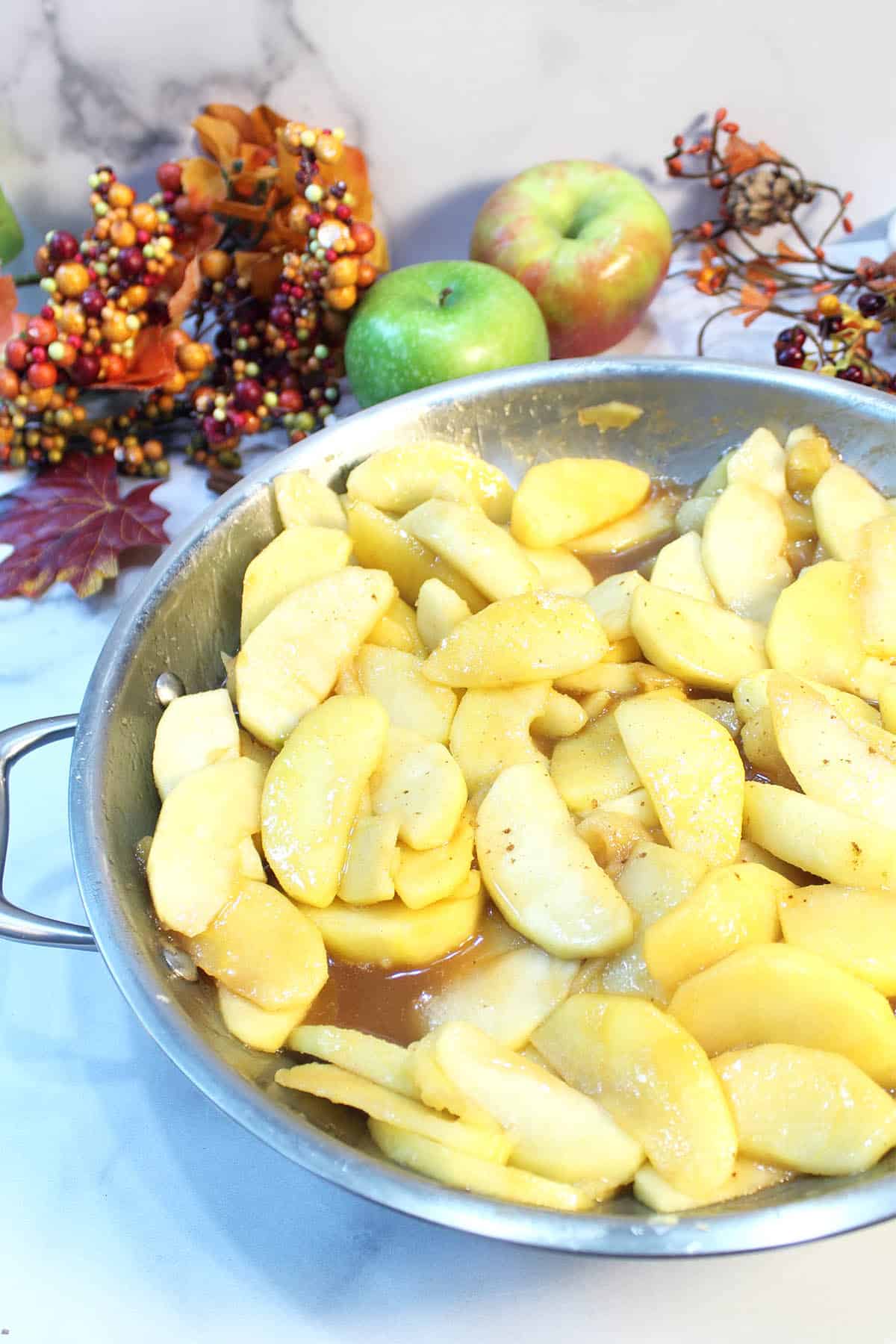 Partial view of skillet with cooked apples with fall foliage in back.