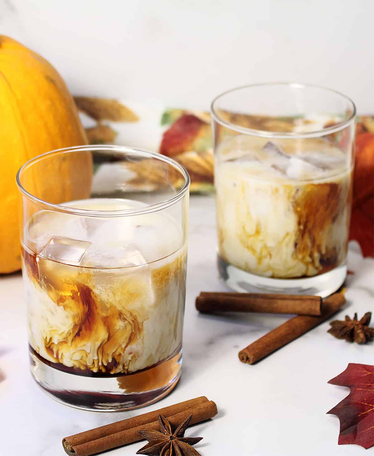 Two Pumpkin Spice White Russian cocktails on table with cinnamon sticks.