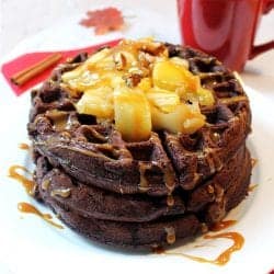 Stack of waffles on white plate with sauteed apples and caramel sauce over top.