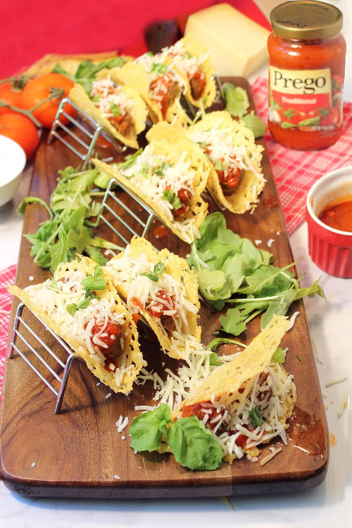 Tacos served in taco stands on wooden board with Prego sauce in background.