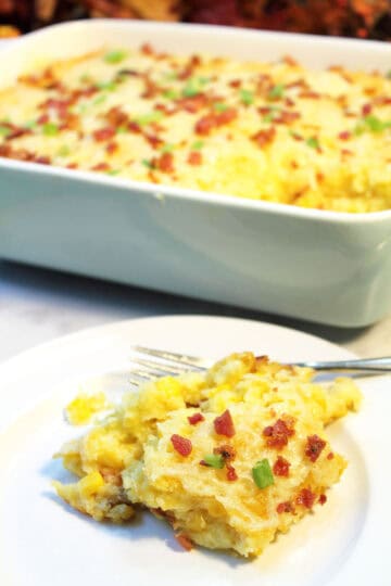 Serving of cheesy corn pudding on white plate with casserole in back.